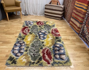 May include: A colorful, abstract rug with a floral design in shades of blue, red, yellow, and green. The rug has a shaggy texture and is made of wool.