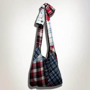 Może przedstawiać: Torba typu tote wykonana z patchworku z różnych tkanin w kratę w odcieniach czerwieni, błękitu i bieli. Torba ma jeden pasek i jest związana u góry pasującą tkaniną.