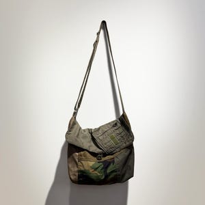 May include: Olive green and camouflage messenger bag with a long shoulder strap. The bag features a flap closure, a front pocket with a button, and a patch pocket. The bag is made of durable, military-style fabric.