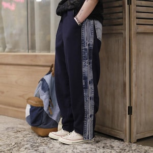 Könnte beinhalten: Eine Person trägt eine dunkelblaue Jogginghose mit einem Jeansstreifen an der Seite. Sie trägt weiße Turnschuhe und hat einen blau-braunen Rucksack auf der Schulter.