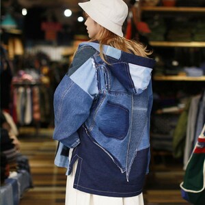 Può includere: Una giacca di jeans blu con cappuccio, realizzata con diversi pezzi di denim cuciti insieme. La giacca ha un design patchwork ed è indossata da una persona con un cappello bianco.