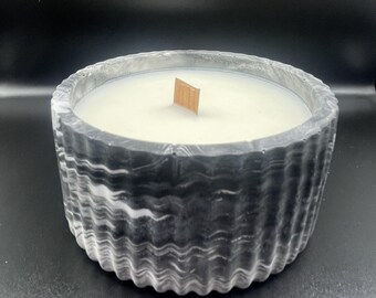 May include: A round candle in a black and white marbled container. The candle has a light-colored wax and a wooden wick. The container has a wavy, textured design.