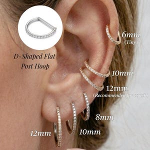 May include: D-shaped flat post hoop earrings featuring clear stones set along the band. The image displays various sizes including 6mm, 8mm, 10mm, and 12mm, showcasing how these metallic hoops appear when worn in different ear piercings.