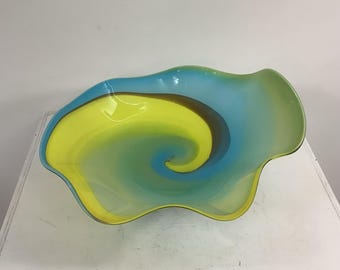 Könnte beinhalten: Eine dekorative Glasschale mit einem wirbelnden Muster in leuchtendem Gelb, Türkisblau und Dunkelbraun. Die Schale hat einen organischen, asymmetrischen und gewellten Rand mit einer glatten, durchscheinenden Oberfläche über das gesamte Stück.