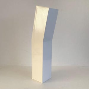 May include: A tall, white, glossy ceramic vase with a distinct angular bend in its vertical structure. The object features a smooth, reflective surface and a rectangular base that tapers slightly as it rises, creating a geometric silhouette.