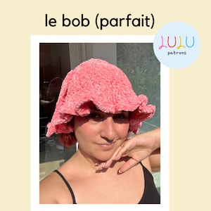 Peut inclure: Un chapeau bob en crochet rose avec un bord festonné. Le chapeau est porté par une personne avec un débardeur noir. Le texte "le bob (parfait)" et "lulu patrons" est visible sur l'image.