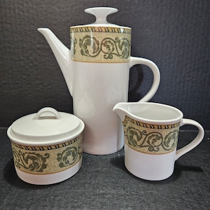 May include: A white ceramic tea set with a green and gold floral design. The set includes a teapot, creamer, and sugar bowl.