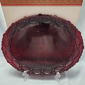 May include: A deep red glass serving plate with a decorative, raised, scalloped edge. The plate has a textured, radial pattern on the surface.