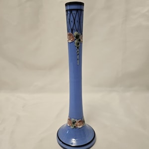 May include: A slender, light blue vase with a flared base and a narrow neck. The vase features a black rim and decorative floral and geometric patterns in pink, green, and black. The vase is approximately 10 inches tall.