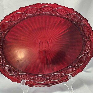 May include: A red glass serving platter with a scalloped edge and a raised, embossed design. The platter has a sunburst pattern in the center.