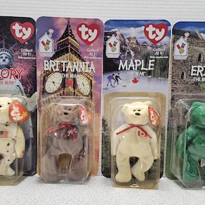 May include: Four Ty Beanie Baby plush toys in their original packaging. The toys are named Glory, Britannia, Maple, and Erin. Each toy is a different color and has a different design. The packaging is white with red and blue accents.