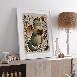 May include: A framed print featuring a whimsical illustration of a green dragon reading a book. The dragon is surrounded by colorful flowers and foliage. The artwork has a soft, watercolor style and is set in a white frame, perfect for a nursery or children's room.