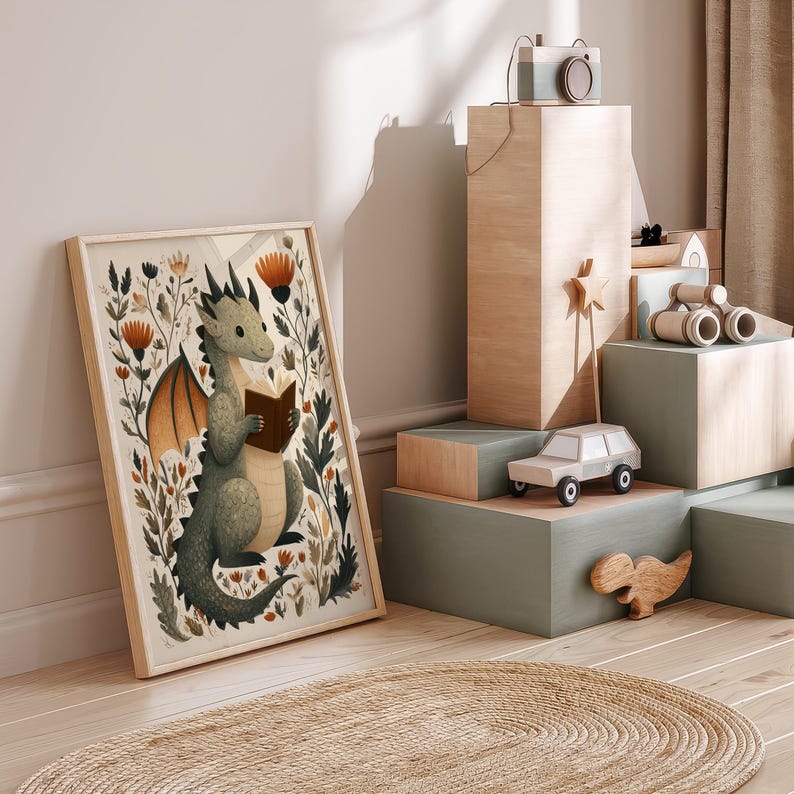 May include: A framed print featuring a whimsical illustration of a green dragon reading a book amidst floral elements. The artwork has a light wood frame and is displayed near wooden toy blocks and a toy car. The color palette includes greens, browns, and oranges.