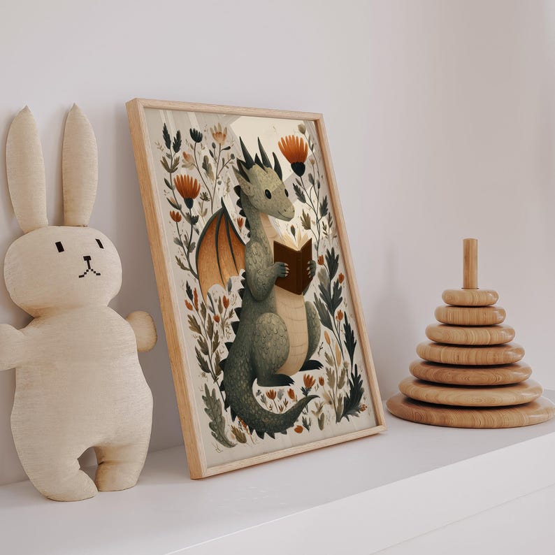 May include: A framed print featuring a whimsical illustration of a green dragon reading a book, surrounded by floral elements. The dragon has orange wings and is set against a neutral background. A plush bunny and a wooden stacking toy are also visible.