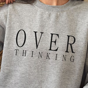 Puede incluir: Sudadera gris con el texto "OVER THINKING" impreso en negro.