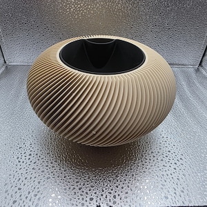 May include: A spherical planter with a beige exterior featuring a series of thin, diagonal, spiraling ridges that wrap around the entire body. The top opening is circular and lined with a smooth, matte black interior insert for holding plants.