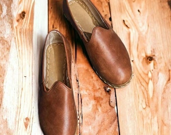 May include: A pair of brown leather slip-on shoes with a pointed toe and a stitched seam around the edge.