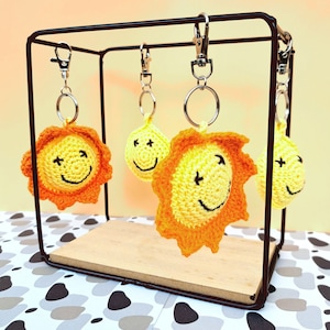 Peut inclure: Quatre breloques en crochet en forme de soleil jaune avec des rayons orange suspendus à des porte-clés argentés sur un présentoir en métal noir.