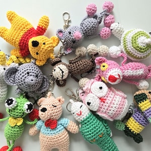Puede incluir: Una colección de llaveros de animales de crochet en varios colores, incluyendo rosa, verde, marrón, amarillo y gris. Los llaveros presentan una variedad de animales, como una rana, un oso, un búho, un unicornio, un mono, un gato, un perro y un pingüino.