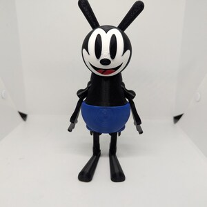 May include: A 3D-printed figure of a cartoon character with a black body, long ears, and a white face with a smiling expression. The character has a blue lower body and black limbs. The figure is standing upright.