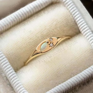Op de afbeelding: Een gouden ring met een witte opaal en twee kleine diamanten, gezet in een delicate ovale vorm. De ring ligt in een wit fluwelen doosje.