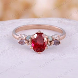 May include: A rose gold ring with a large oval ruby gemstone surrounded by smaller white and purple gemstones. The ring is set on a white background.
