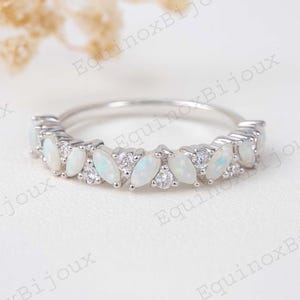 May include: A silver ring featuring a row of marquise-cut opals and small round diamonds. The opals are white with a subtle play of color, and the diamonds sparkle. The ring is set on a delicate band, perfect for everyday wear or special occasions.