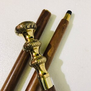 May include: A wooden walking stick with a brass handle featuring intricate floral designs. The handle has a decorative, textured pattern and a black rubber tip.