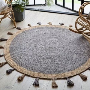 May include: A round jute rug with a gray center and a natural jute border. The rug has tassels around the edge.