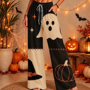 May include: Black and beige wide-leg pants featuring a drawstring waist, a large ghost applique on the right leg, a witch hat applique on the left leg, and an orange pumpkin outline on the lower right leg with small star accents.