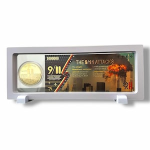 May include: A gold-colored commemorative coin in a clear plastic display case with a black and gold background featuring the text "9/11 NEVER FORGET SEPTEMBER 11, 2001" and an image of the Twin Towers. The background also features the text "THE 9/11 ATTACKS" and a depiction of the Twin Towers on fire.