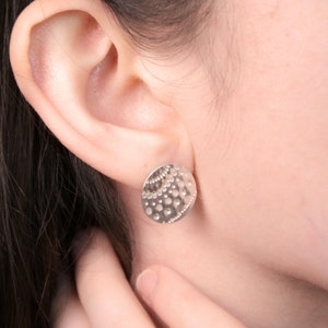 Könnte beinhalten: Nahaufnahme eines Ohrs mit einem silbernen Ohrstecker mit einem strukturierten runden Design.