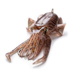 Könnte beinhalten: Ein brauner, durchscheinender Angelköder in Tintenfischform mit dunkelbraunen Flecken, markanten Augen und mehreren Tentakeln. Ein scharfer Metallhaken ist in die Unterseite des Körpers integriert und eine kleine Metallöse befindet sich oben.