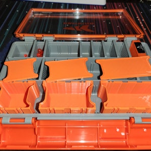 May include: A gray and orange tackle box with a clear lid. The box is open, revealing several orange compartments and dividers. The box is designed to store small items, such as fishing lures or craft supplies.