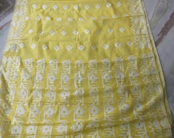 May include: A yellow textile with white geometric patterns. The fabric is folded and spread out, showcasing a repeating design of diamond shapes and stylized floral motifs. The edges are finished with a detailed border.
