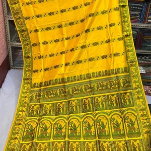 May include: A bright yellow saree featuring horizontal rows of small dark green animal motifs. The wide border displays intricate green and dark red panels with repeating illustrations of figures in various poses, framed by decorative geometric patterns.