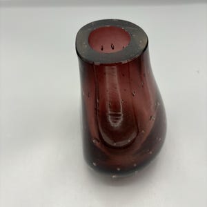 Peut inclure: Un petit vase en verre de couleur violet foncé avec un corps rond en forme de poire. Le vase a une surface texturée avec de petites bulles d'air partout.