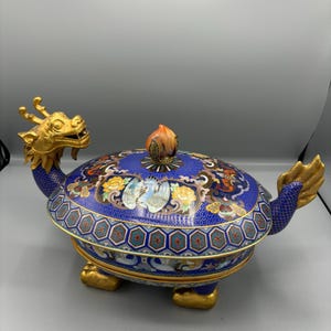 May include: A blue and gold cloisonné dragon and turtle incense burner with a floral design. The lid has a peach-shaped finial.