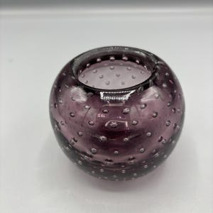 May include: A round, purple glass vase with a bubble design. The vase is a deep shade of purple and has a wide opening. The glass has a textured appearance due to the embedded bubbles. The vase is suitable for decorative purposes.