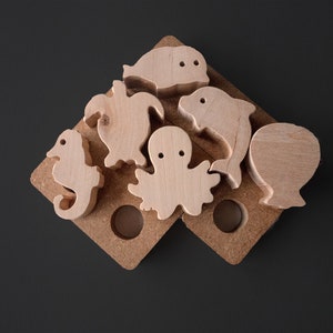 Peut inclure: Puzzle en bois avec des créatures marines, dont un dauphin, une pieuvre, un hippocampe, une tortue et un poisson. Les pièces sont disposées sur une base en bois avec des découpes pour chaque forme.