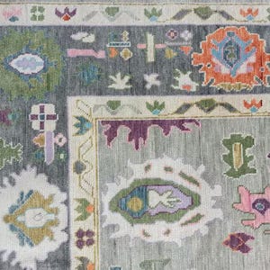 Pu&ograve; includere: Primo piano di un tappeto grigio con un motivo geometrico colorato. Il tappeto ha un bordo con un motivo ripetitivo di fiori e foglie.
