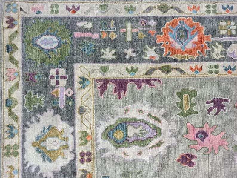 Pu&ograve; includere: Primo piano di un tappeto grigio con un motivo geometrico colorato. Il tappeto ha un bordo con un motivo ripetitivo di fiori e foglie.