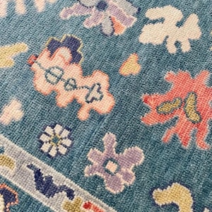 May include: A close-up of a blue rug with a floral pattern. The rug features pink, yellow, white, and purple flowers on a blue background.