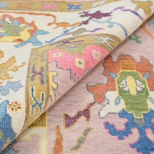 May include: A close-up of a pink and cream rug with a floral pattern. The rug has a detailed design with intricate details in shades of blue, yellow, orange, and purple.