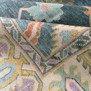 May include: Close-up of a patterned rug with a cream background and a blue, pink, and yellow floral design.