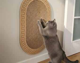Könnte beinhalten: Ein ovaler, an der Wand montierter Kratzbaum für Katzen mit einer zentralen, strukturierten Sisalseiloberfläche, umgeben von einem hellen Holzrahmen mit einem sich wiederholenden geometrischen Mäander-Muster am Rand.