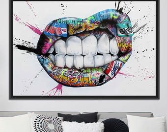 May include: A framed artwork featuring a close-up of a mouth with large, white teeth. The lips are covered in colorful graffiti art, with splashes of pink and black paint on a white background. The word "HELLO" is visible on a tag.