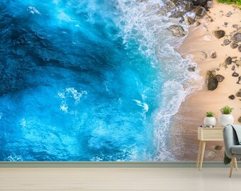 May include: An aerial view of a sandy beach with turquoise blue water crashing on the shore. The beach is lined with rocks and green vegetation.