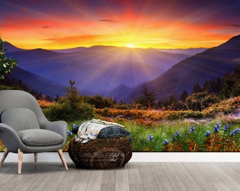May include: A wall mural showing a mountain landscape at sunset. The image includes a grey armchair, a woven basket, and a potted tree. The sunset sky transitions from orange to blue, with mountains in the background.