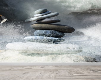 May include: A stack of smooth, gray stones balanced on top of each other in a zen-like formation. The stones are set against a backdrop of a rushing river with white water and a misty, gray sky.